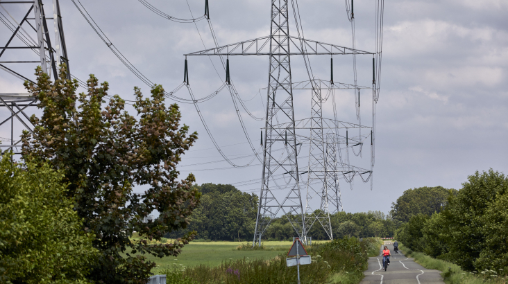 hoogspanningsmast met een weg erlangs waar fietsers fietsen